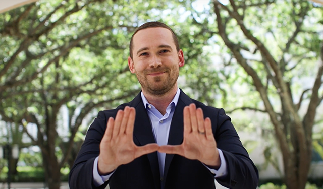 MAIA alumni holding up his hands in the "UM" symbol. 