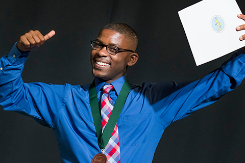 A happy student gives a thumbs up and holds up his certificate in the other hand. 